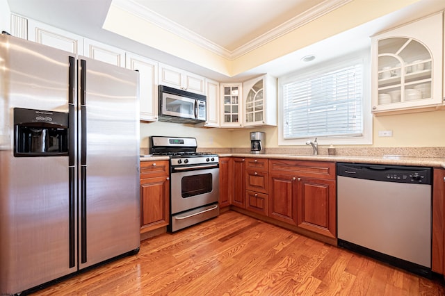 kitchen with sink, light wood-type flooring, ornamental molding, appliances with stainless steel finishes, and a tray ceiling