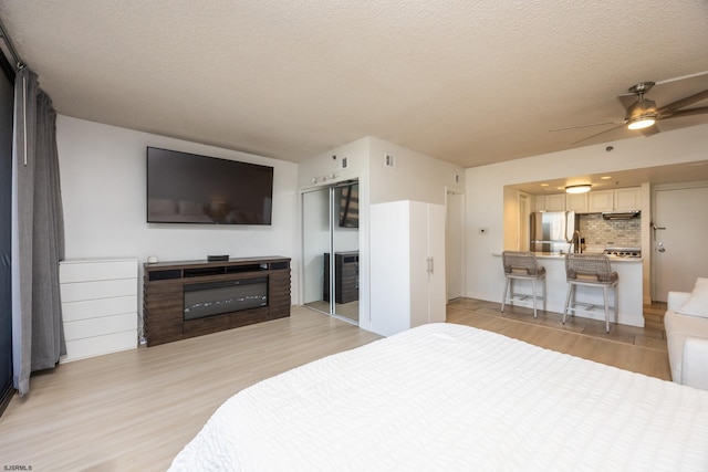 bedroom with ceiling fan, a textured ceiling, light hardwood / wood-style floors, stainless steel refrigerator, and a closet