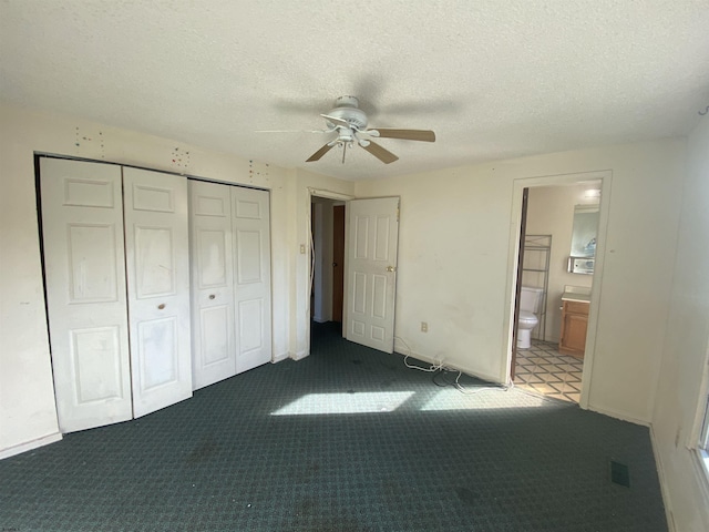 unfurnished bedroom with dark colored carpet, ceiling fan, a textured ceiling, and connected bathroom