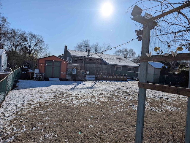 snow covered house with a storage shed, an outbuilding, and fence