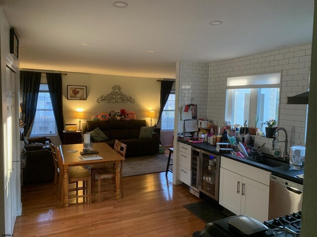kitchen featuring light wood-style flooring, wine cooler, a sink, stainless steel dishwasher, and dark countertops