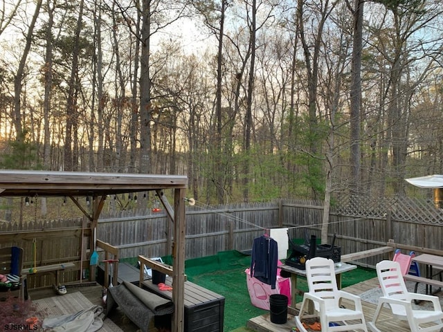 view of patio / terrace featuring a view of trees, a wooden deck, and a fenced backyard