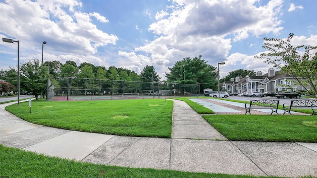 view of property's community featuring a lawn and tennis court