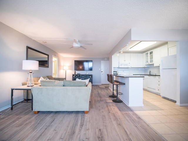 living room featuring ceiling fan, sink, a textured ceiling, and light hardwood / wood-style flooring