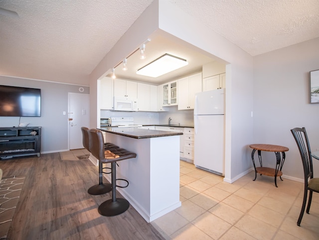 kitchen featuring white cabinetry, sink, a textured ceiling, white appliances, and a breakfast bar area