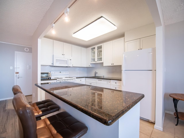 kitchen featuring white appliances, sink, a textured ceiling, a kitchen bar, and white cabinetry