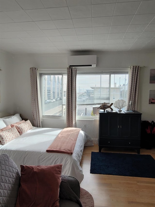 bedroom with an AC wall unit, light hardwood / wood-style flooring, and multiple windows