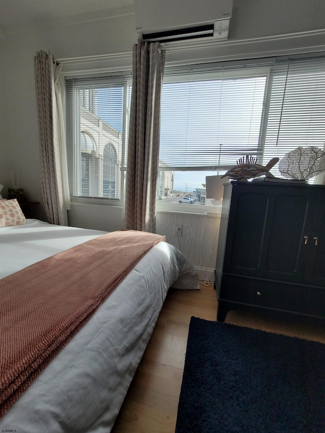 bedroom featuring a wall mounted air conditioner, hardwood / wood-style floors, and multiple windows