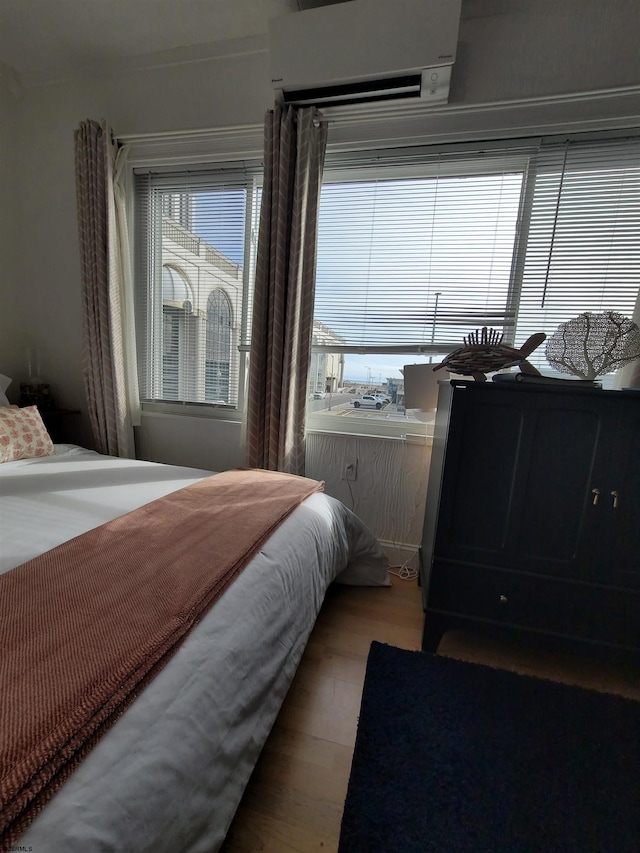 bedroom featuring wood-type flooring, an AC wall unit, and multiple windows