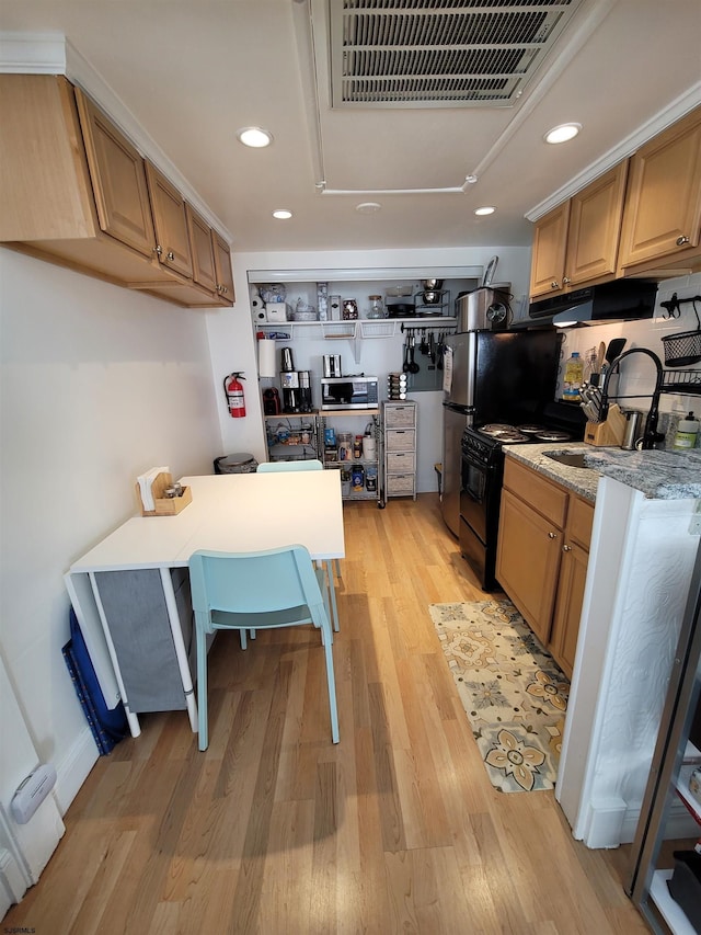 kitchen with black electric range, light hardwood / wood-style floors, light stone countertops, and sink