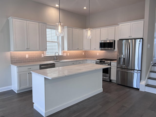 kitchen featuring stainless steel appliances, sink, pendant lighting, white cabinets, and a kitchen island