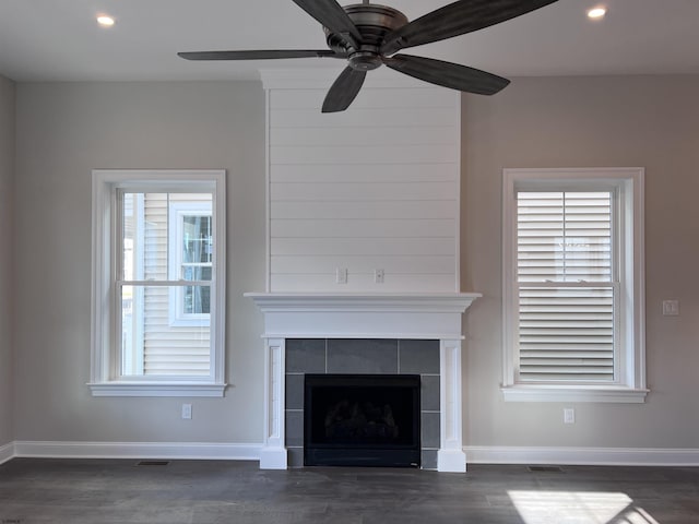 unfurnished living room with dark hardwood / wood-style flooring, ceiling fan, and a tiled fireplace