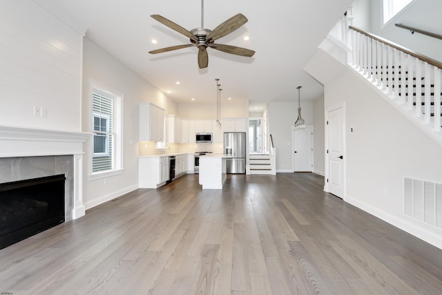 unfurnished living room featuring a tiled fireplace, ceiling fan, sink, and hardwood / wood-style flooring