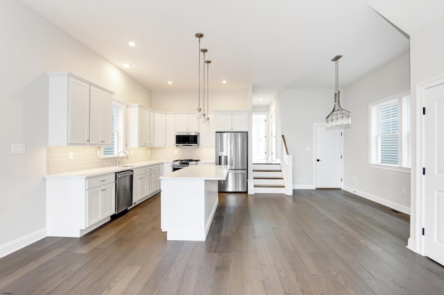 kitchen with white cabinets, decorative light fixtures, a center island, and appliances with stainless steel finishes