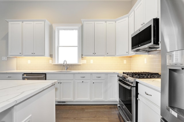 kitchen with white cabinets, sink, light stone countertops, and stainless steel appliances