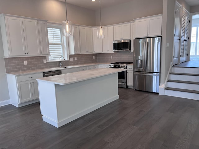 kitchen with sink, stainless steel appliances, a kitchen island, decorative light fixtures, and white cabinets