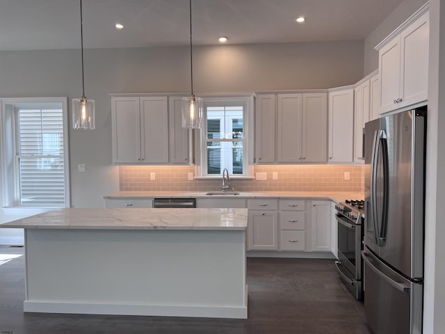 kitchen with a center island, white cabinets, light stone countertops, decorative light fixtures, and stainless steel appliances