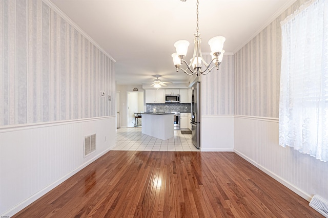 unfurnished living room featuring ceiling fan with notable chandelier, light hardwood / wood-style floors, and crown molding