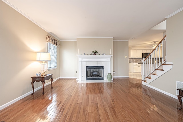 living room featuring light wood-type flooring, crown molding, and a tile fireplace