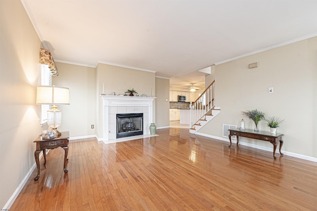 living room with a tile fireplace, ceiling fan, ornamental molding, and hardwood / wood-style flooring