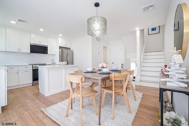 kitchen with pendant lighting, white cabinets, decorative backsplash, light wood-type flooring, and stainless steel appliances