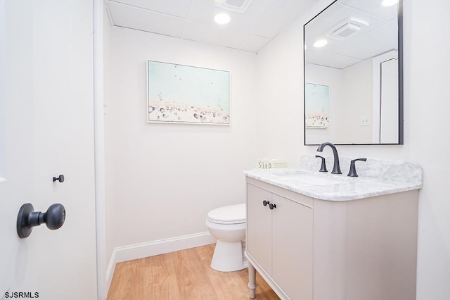 bathroom with toilet, vanity, a drop ceiling, and hardwood / wood-style flooring