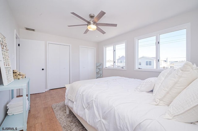 bedroom with ceiling fan, light hardwood / wood-style floors, and two closets