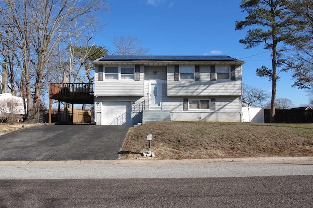 bi-level home with solar panels, a garage, and a wooden deck