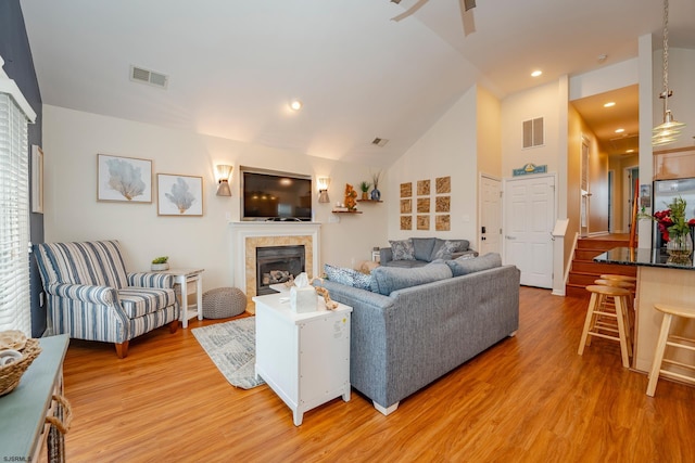 living room with wood-type flooring, high vaulted ceiling, and a tiled fireplace