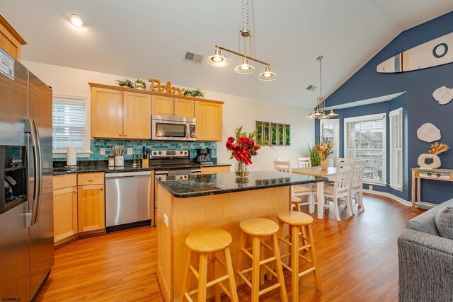 kitchen with decorative backsplash, appliances with stainless steel finishes, decorative light fixtures, a center island, and lofted ceiling