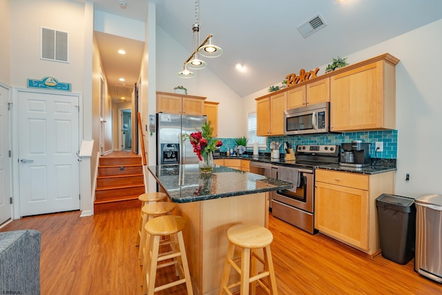 kitchen featuring a center island, a kitchen breakfast bar, decorative backsplash, light brown cabinetry, and appliances with stainless steel finishes