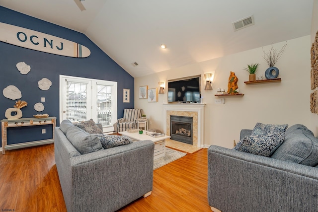 living room featuring lofted ceiling, wood-type flooring, and a tiled fireplace