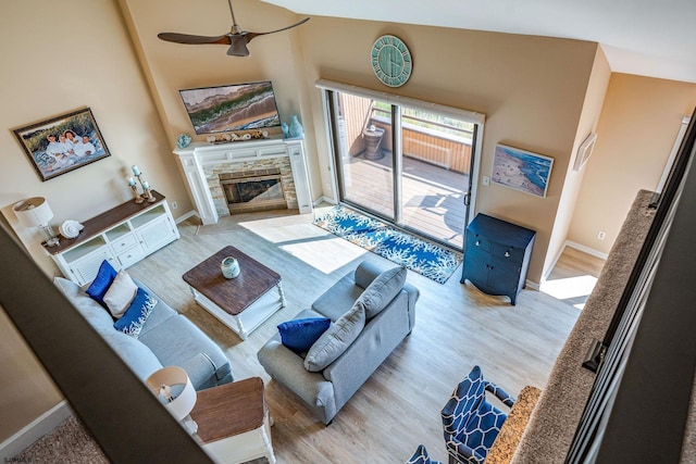 living room featuring lofted ceiling, ceiling fan, a stone fireplace, and light wood-type flooring