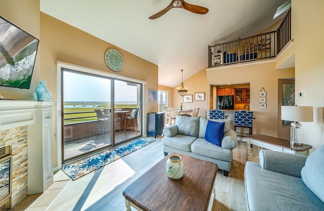 living room with ceiling fan, a stone fireplace, high vaulted ceiling, and light hardwood / wood-style flooring