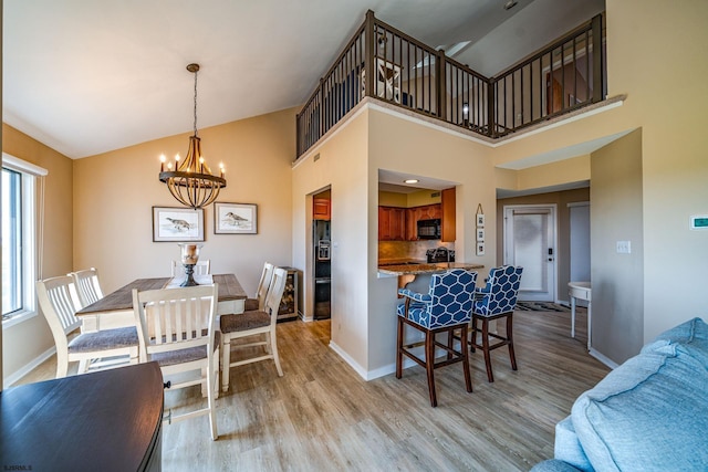 dining space with high vaulted ceiling, light hardwood / wood-style flooring, a wealth of natural light, and a notable chandelier