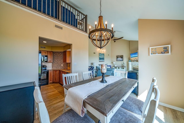 dining space with a stone fireplace, high vaulted ceiling, a chandelier, and light wood-type flooring