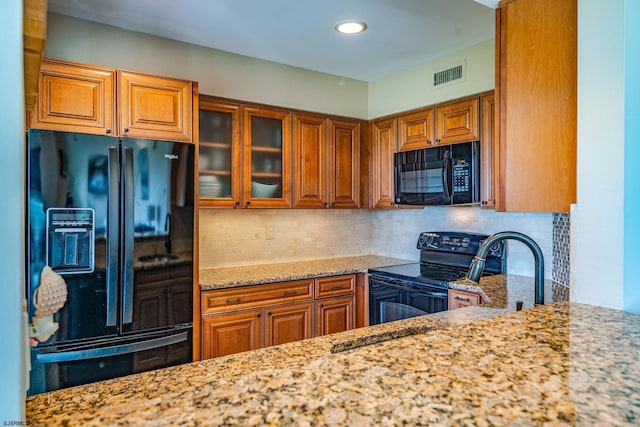 kitchen with tasteful backsplash, light stone counters, and black appliances