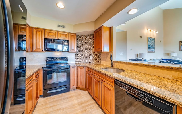 kitchen featuring light stone countertops, tasteful backsplash, sink, black appliances, and light hardwood / wood-style flooring