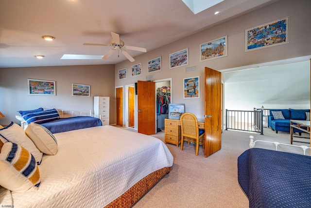 bedroom with a walk in closet, light colored carpet, lofted ceiling with skylight, ceiling fan, and a closet