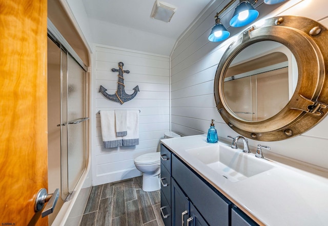 full bathroom featuring vanity, shower / bath combination with glass door, wooden walls, vaulted ceiling, and toilet