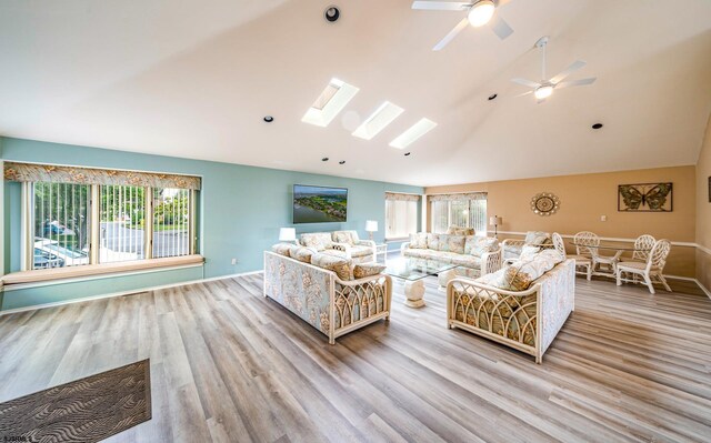 living room with a wealth of natural light, ceiling fan, vaulted ceiling with skylight, and light wood-type flooring