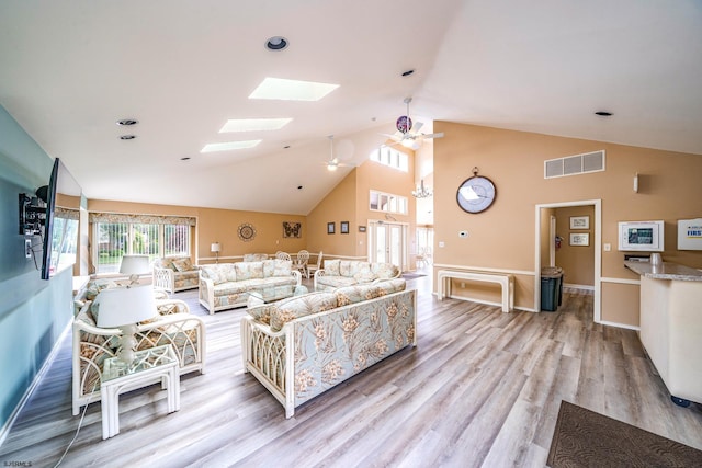 living room with vaulted ceiling with skylight, ceiling fan, and light hardwood / wood-style floors