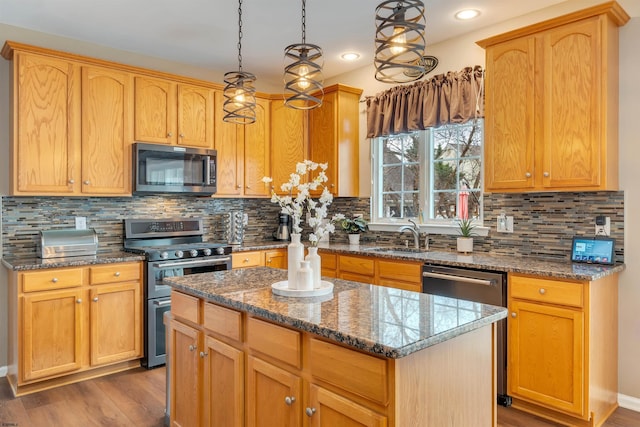 kitchen with sink, hanging light fixtures, stainless steel appliances, stone countertops, and a kitchen island