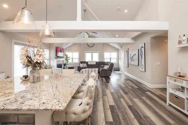 kitchen featuring a breakfast bar area, hanging light fixtures, dark hardwood / wood-style floors, light stone counters, and lofted ceiling with beams