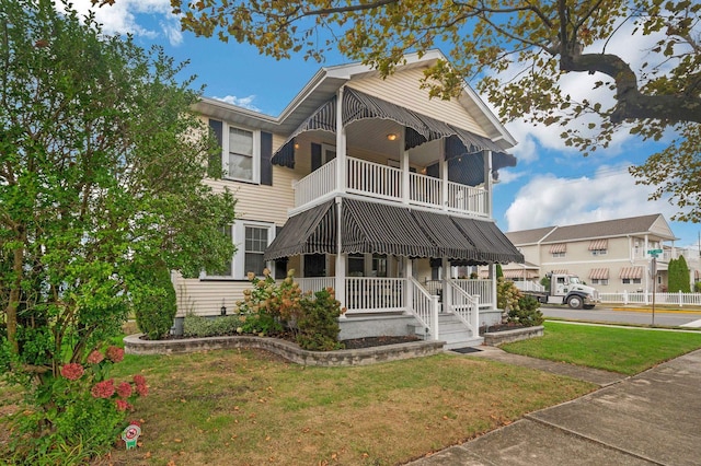 view of front facade featuring a balcony, covered porch, and a front yard