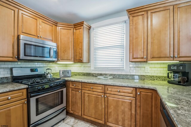 kitchen featuring decorative backsplash, appliances with stainless steel finishes, light stone counters, and a healthy amount of sunlight