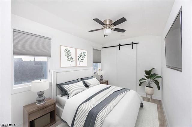 bedroom with ceiling fan, a barn door, and light hardwood / wood-style floors