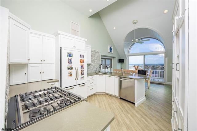 kitchen with high vaulted ceiling, white cabinets, kitchen peninsula, stainless steel appliances, and light hardwood / wood-style flooring