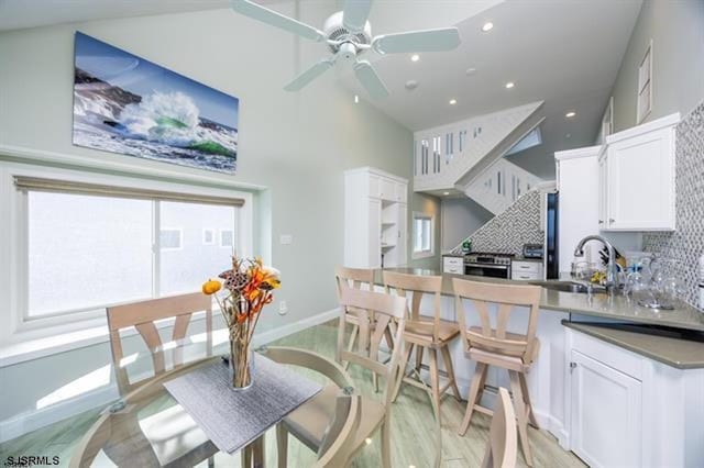 kitchen featuring sink, light wood-type flooring, backsplash, stainless steel stove, and white cabinets