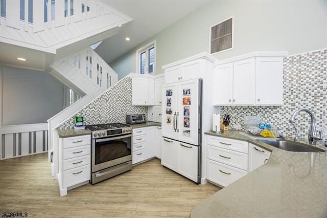 kitchen with built in fridge, sink, white cabinets, and stainless steel range oven